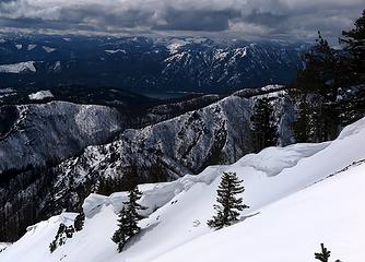 Layers of scenery:  cornices on a ridge line below, burned slopes of the Jolly Creek fire, Cle Elum Lake, Domerie & Baldy beyond the Lake, I-90 clearcuts, and storm clouds out west