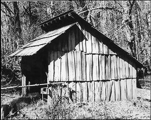 Front corner elevation of Bob Creek Shelter. A can and an identifying sign hang in front of shelter. NPS photo, courtesy of Russ Dalton (RDA.002.023)