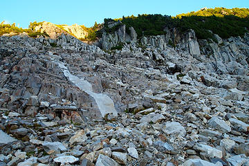 Follow the stripe. There are some cairns marking the way, but you head for the little patch of meadow in the upper center. Look for a small tree with orange flag. Do NOT go left into the meadow when you get there.